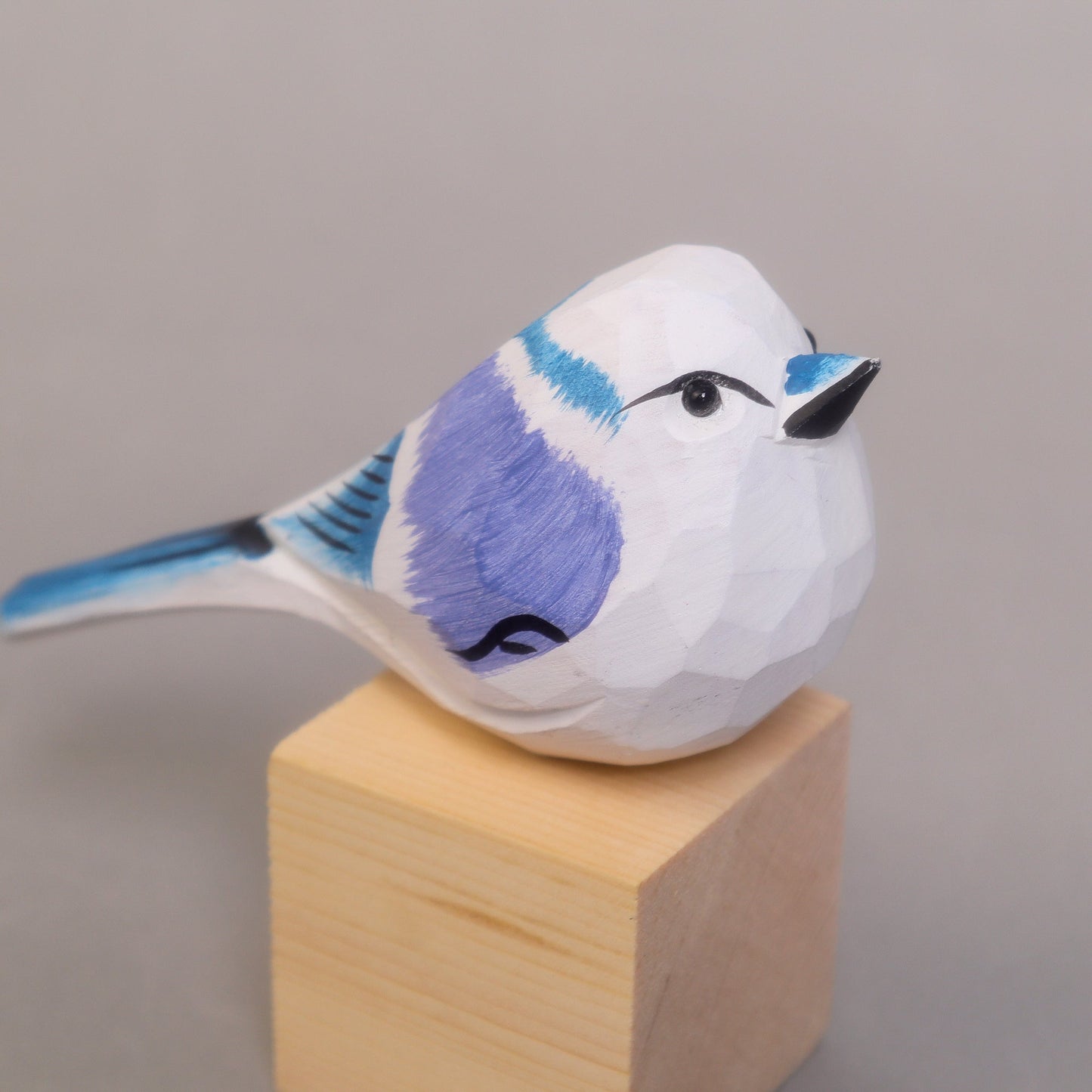 Decorative blue bird figurine with blue and purple details on a wooden block against a gray background