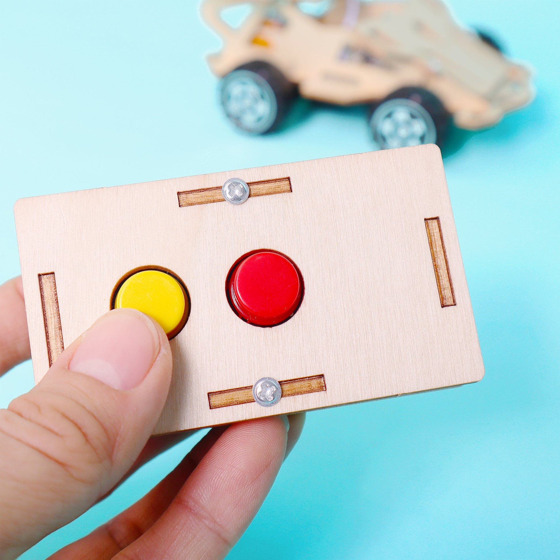 Wooden toy control panel with buttons held by a hand against a blue background