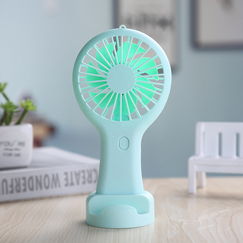 Turquoise handheld fan on a wooden surface with a blurred indoor background