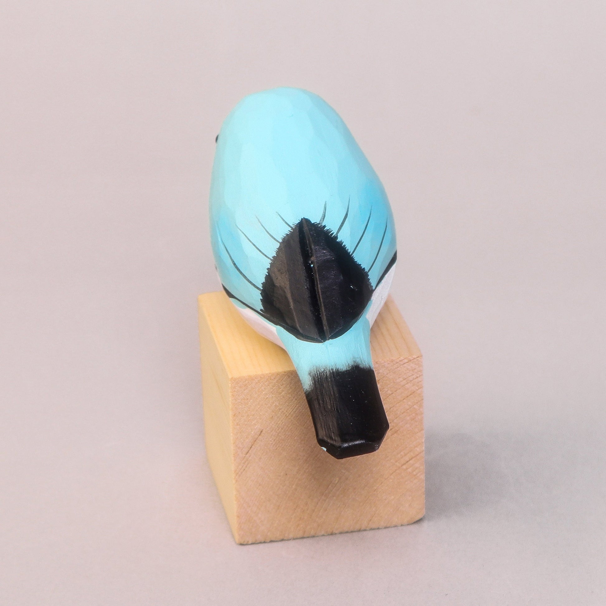 Blue and black bird-shaped figurine on a beige block against a light gray background