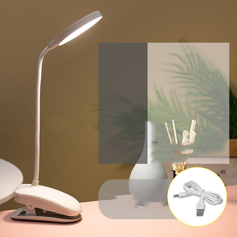 White LED desk lamp with flexible neck on a table, with a plant and decorative items in the background.
