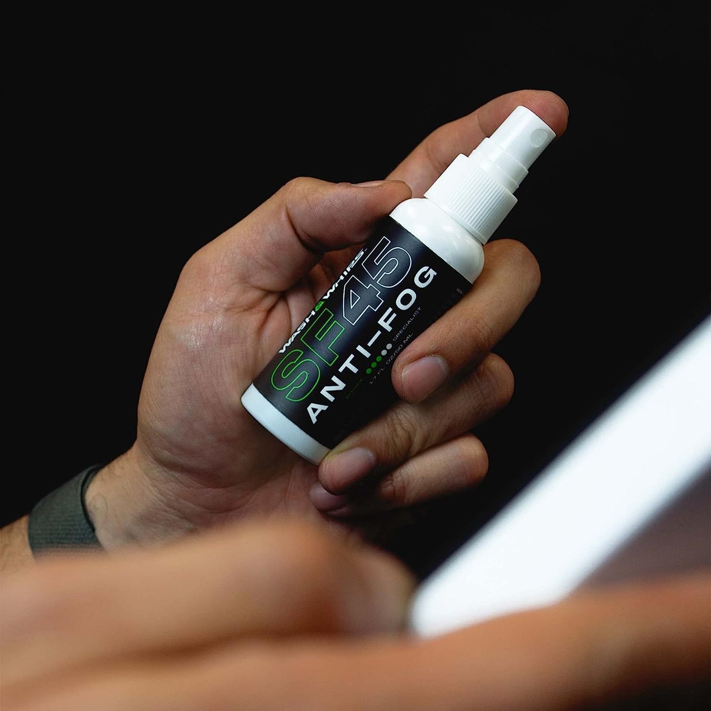 Hand holding a bottle of S45 Anti-Fog spray against a black background
