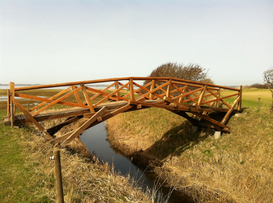 Wooden bridge over a small stream with grassy banks and a clear sky.