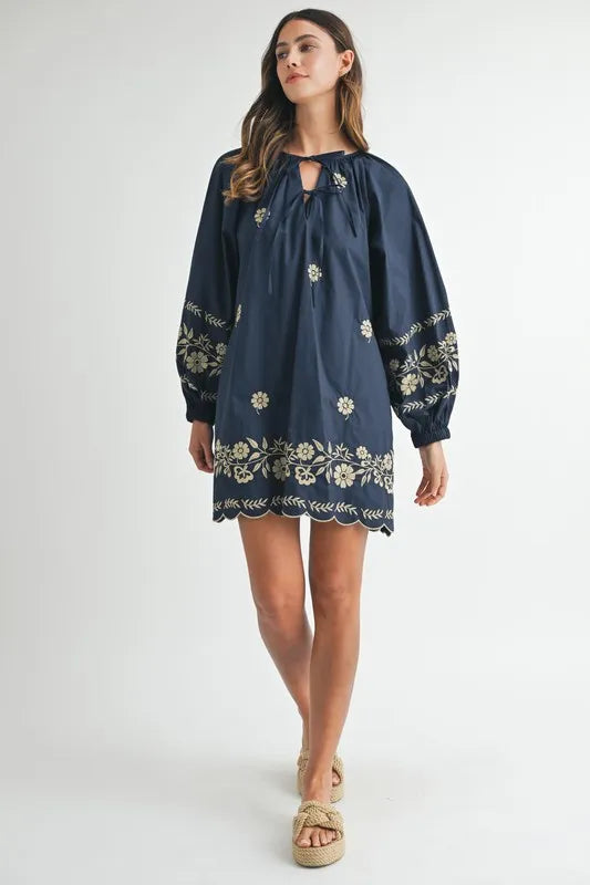 Woman wearing a navy dress with floral embroidery on a white background