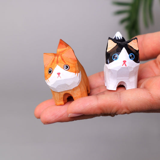 Two small cat figurines held in a hand against a neutral background