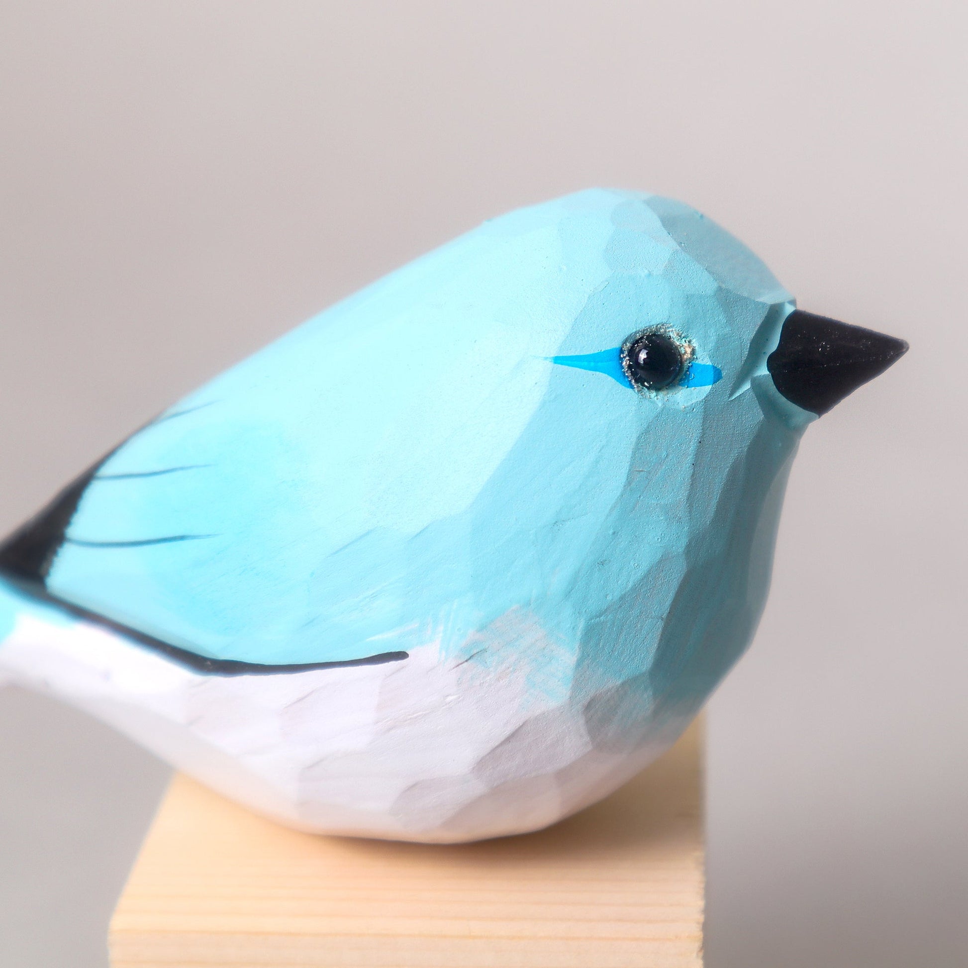 Blue bird figurine on a wooden stand with a plain background