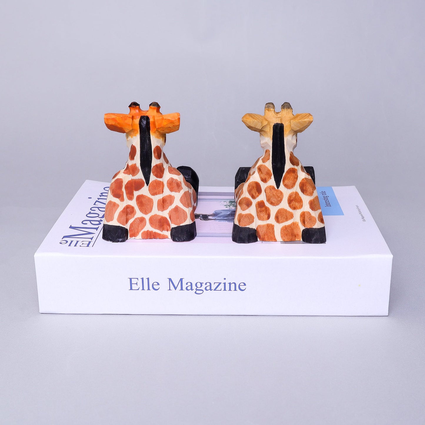 Two giraffe-shaped bookends on top of an Elle Magazine box.