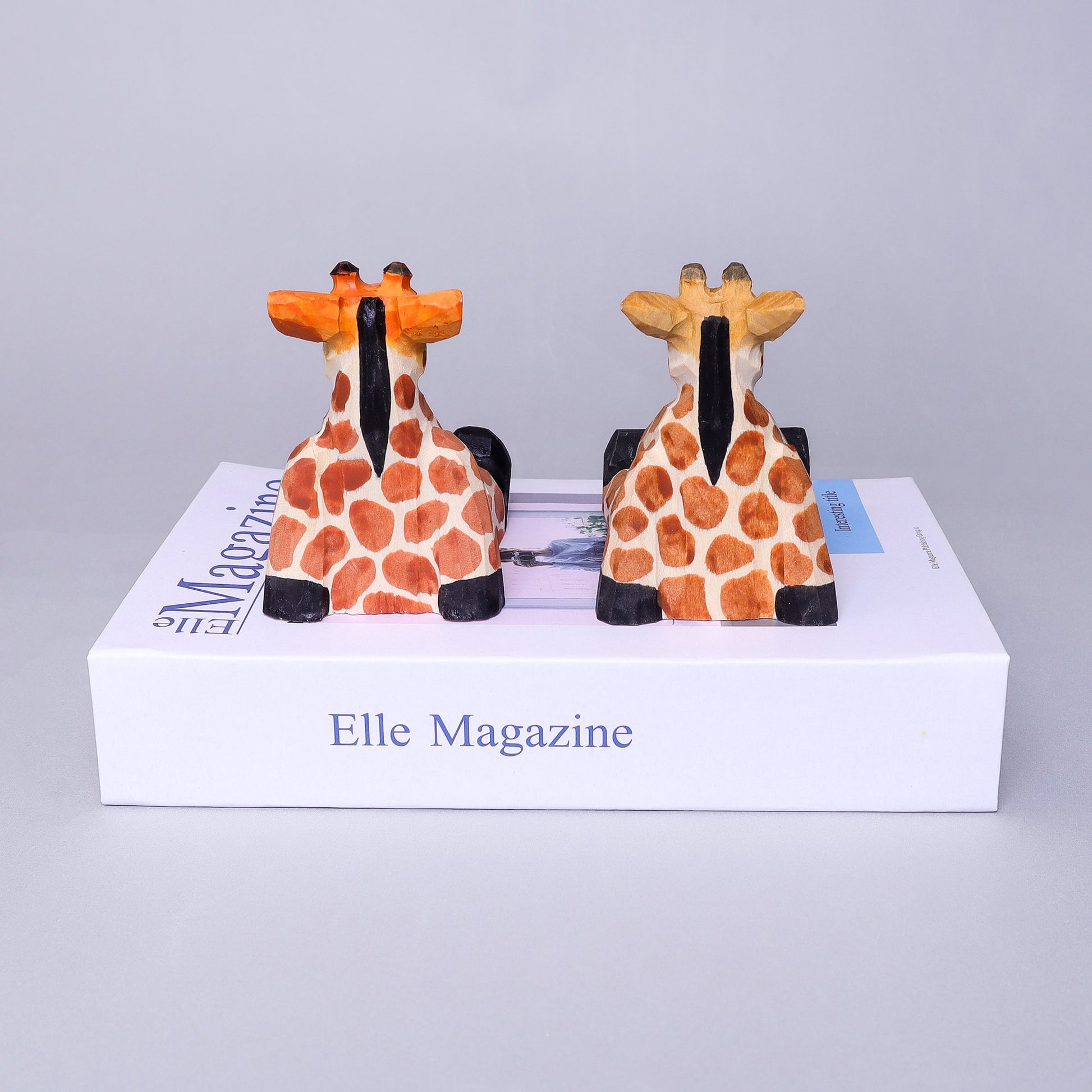 Two giraffe-shaped bookends on top of an Elle Magazine box.
