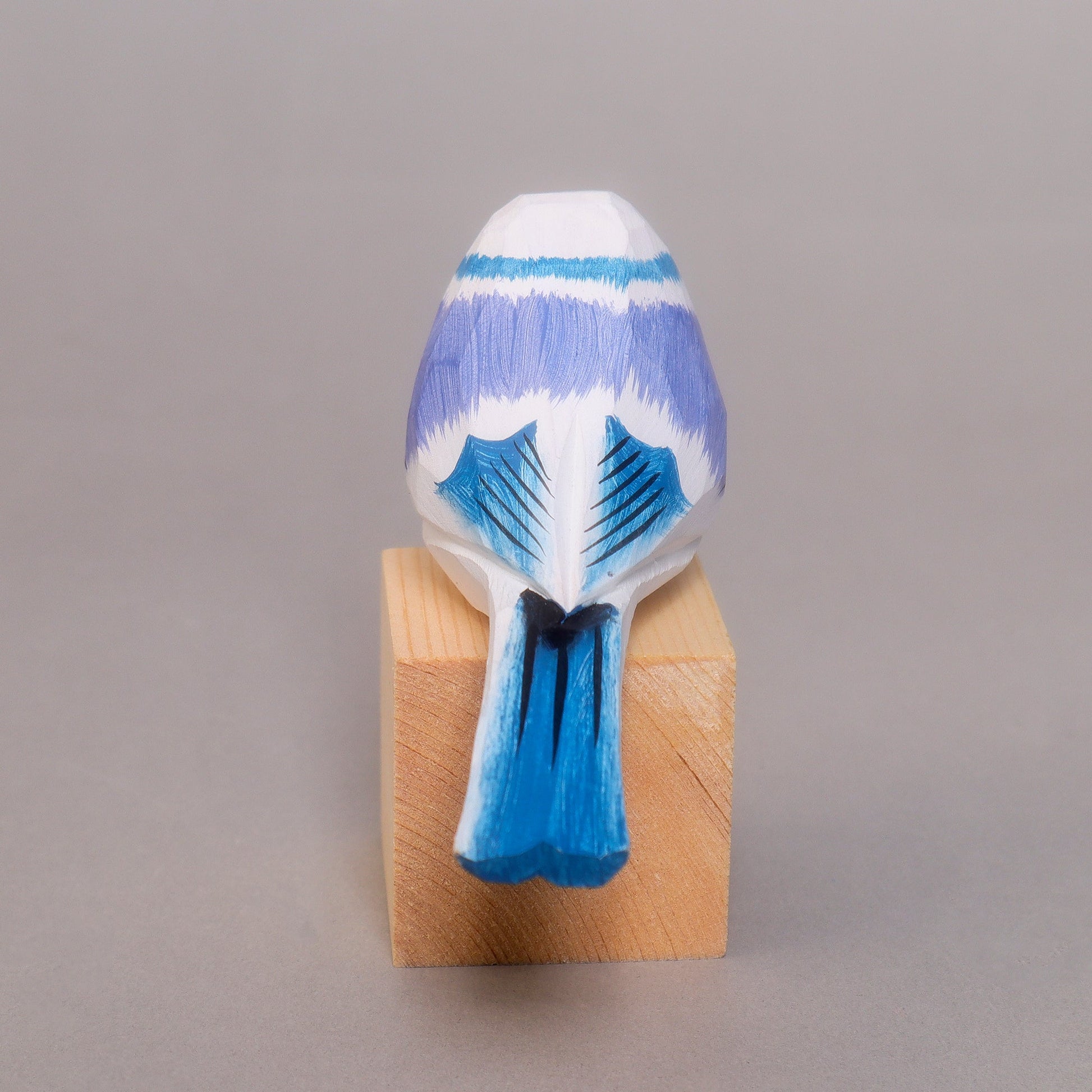 Rear of a Blue and white wood bird figurine on a wooden block against a gray background