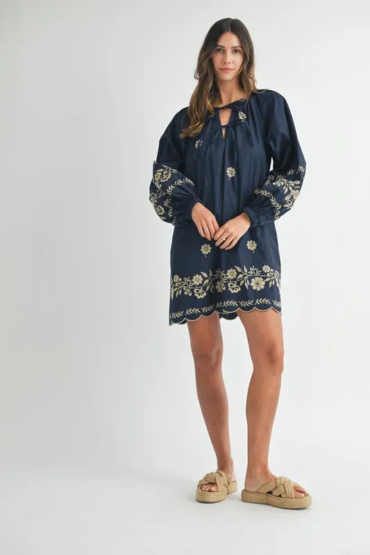 Woman wearing a navy dress with floral embroidery on a white background