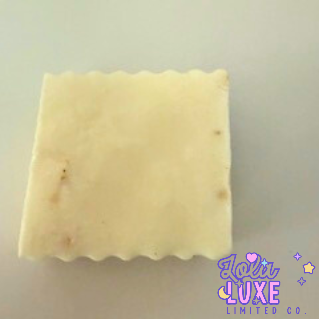 Square bar of soap with visible blemishes on a light background, featuring the brand 'Loli Luxe'.