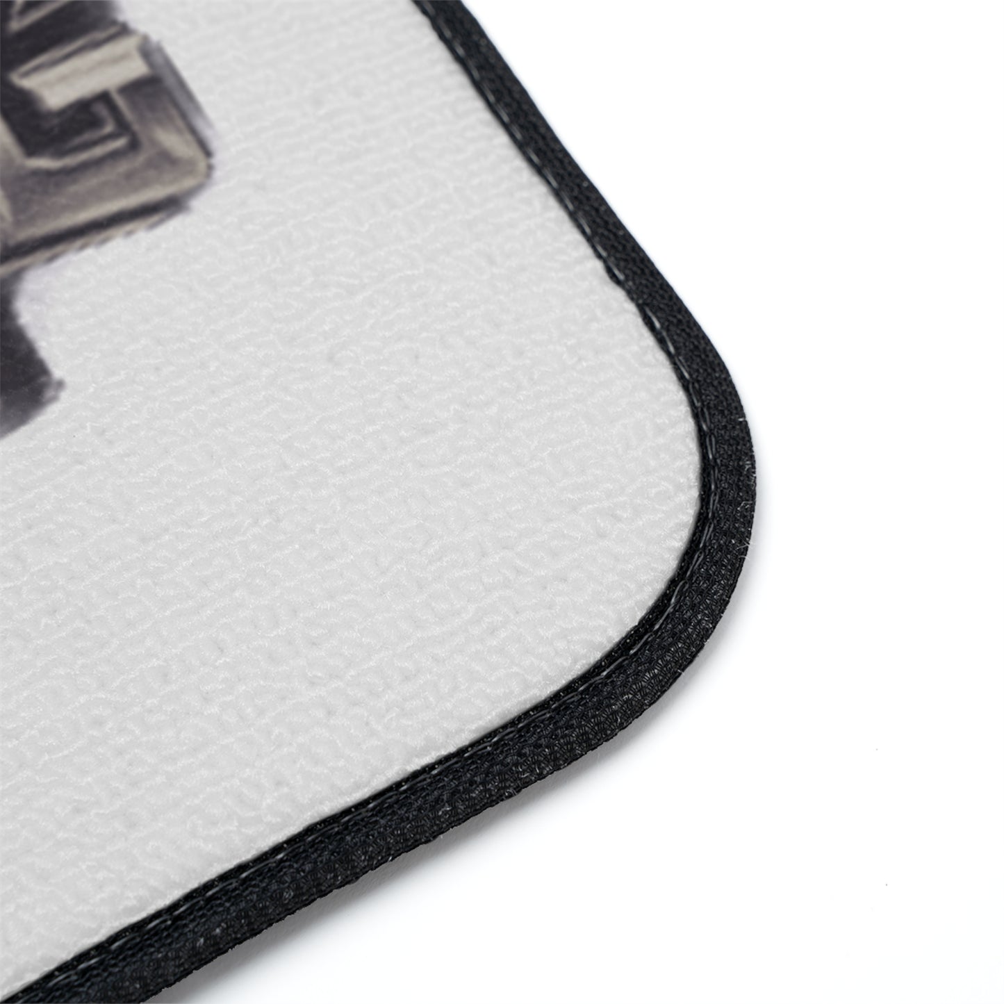 Close-up of a white textured floor mat with a black stitched border, showing part of a black and gray graphic print on a white background.
