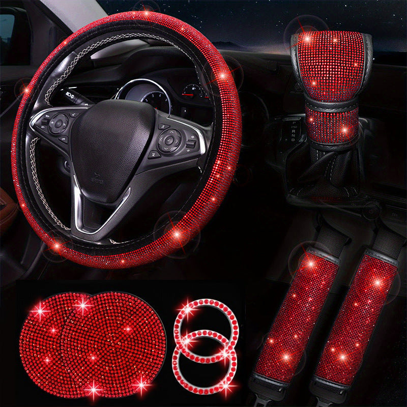 Red rhinestone car interior accessories set including steering wheel cover, gear shift cover, seat cup holders, and ring on a dark background.