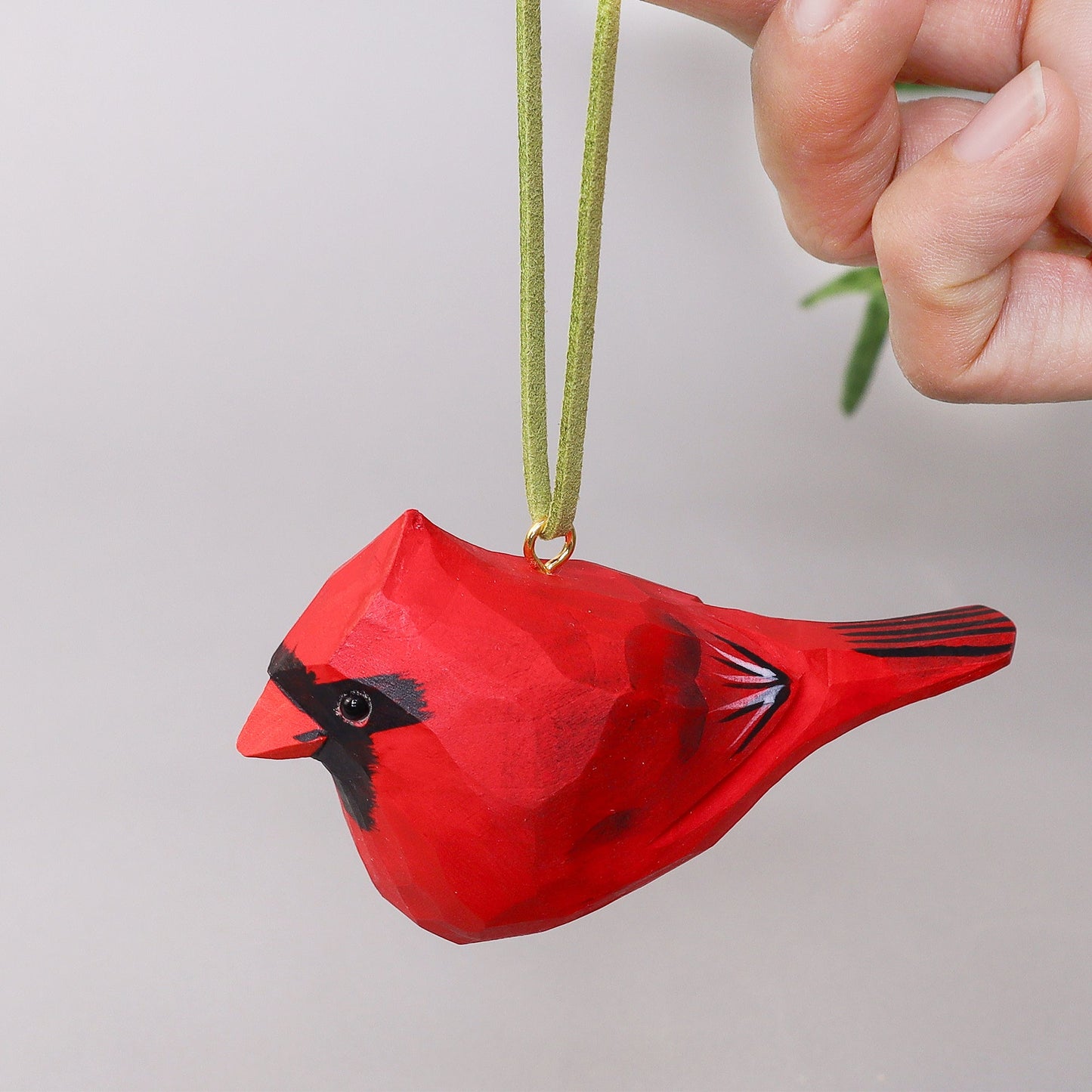 Red cardinal bird ornament hanging from a hand against a neutral background