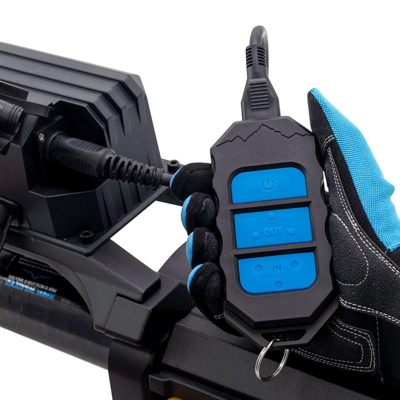 Black remote control with blue buttons attached to a vehicle, held by a gloved hand.