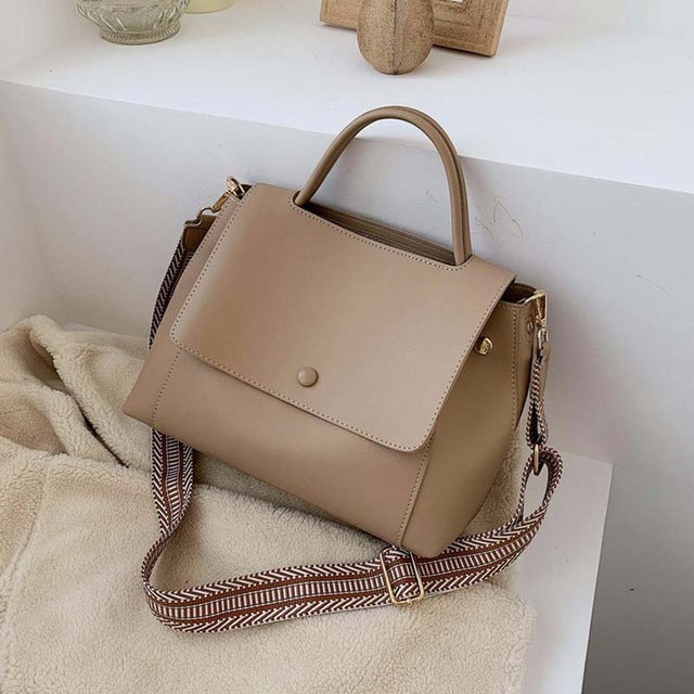 Beige handbag with a patterned strap on a white surface