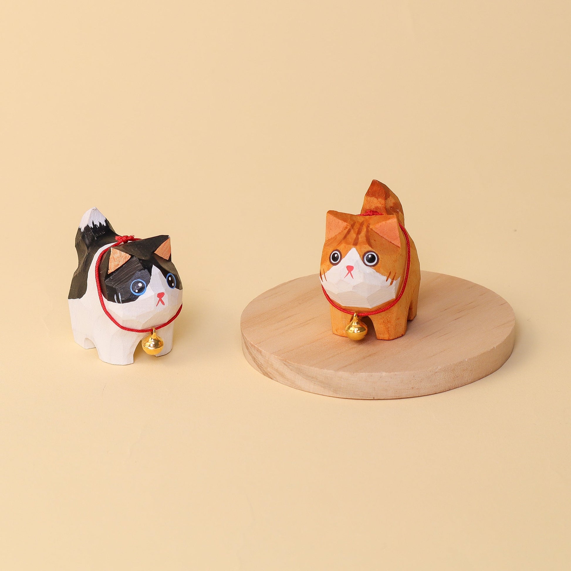 Two cat-shaped figurines with red necklaces on a beige background
