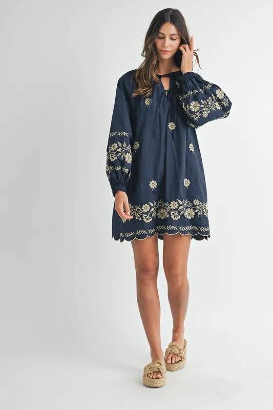 Woman wearing a navy blue dress with floral embroidery on a white background