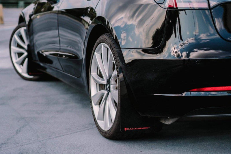 Close-up of a black car's wheel and part of its body on a road.