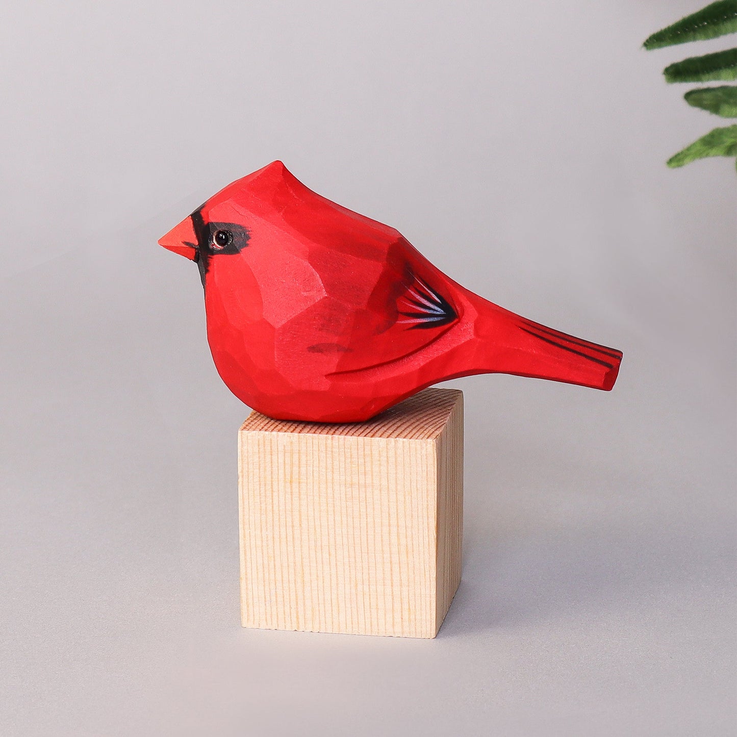 Red cardinal figurine on a wooden block against a gray background