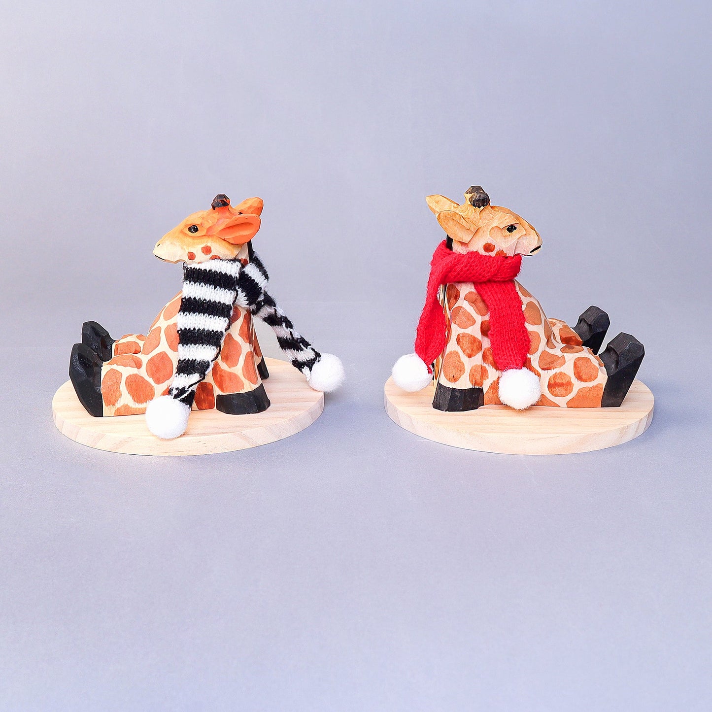 Two decorative giraffe figurines wearing scarves on a light gray background
