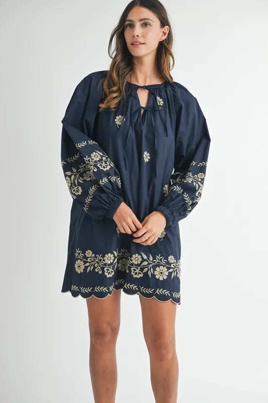 Woman wearing a navy blue dress with floral embroidery on a white background