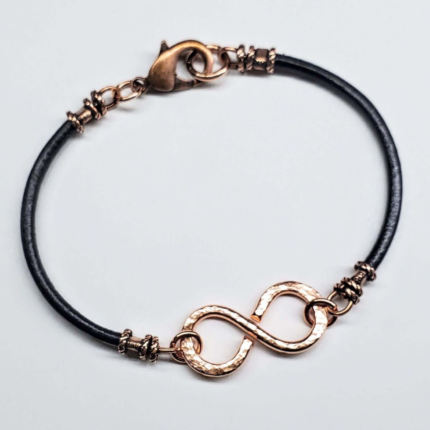 Bracelet with rose gold infinity symbol and black cord on a light gray background