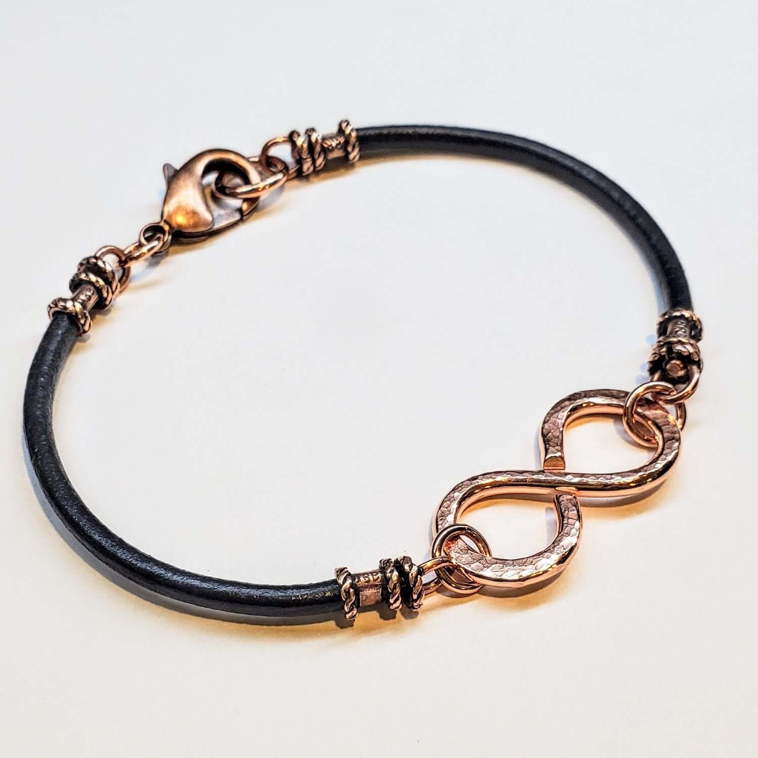 Bracelet with black leather strap and rose gold infinity symbol on a light gray background