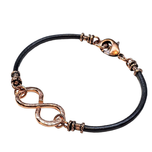 Bracelet with black leather strap and rose gold infinity symbol on a white background