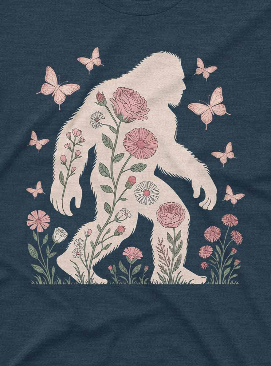 Navy blue t-shirt with a white silhouette of a bigfoot surrounded by flowers and butterflies on a dark fabric background.