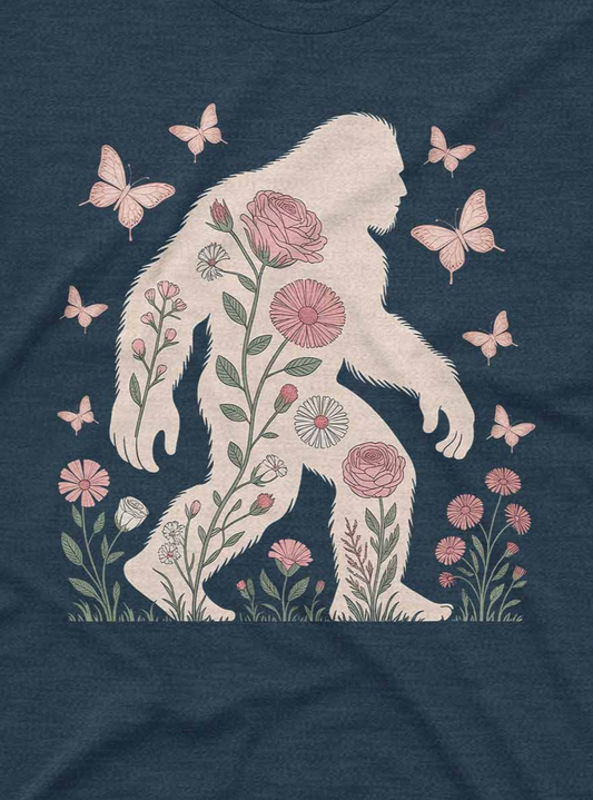 Navy blue t-shirt with a white silhouette of a bigfoot surrounded by flowers and butterflies on a dark fabric background.