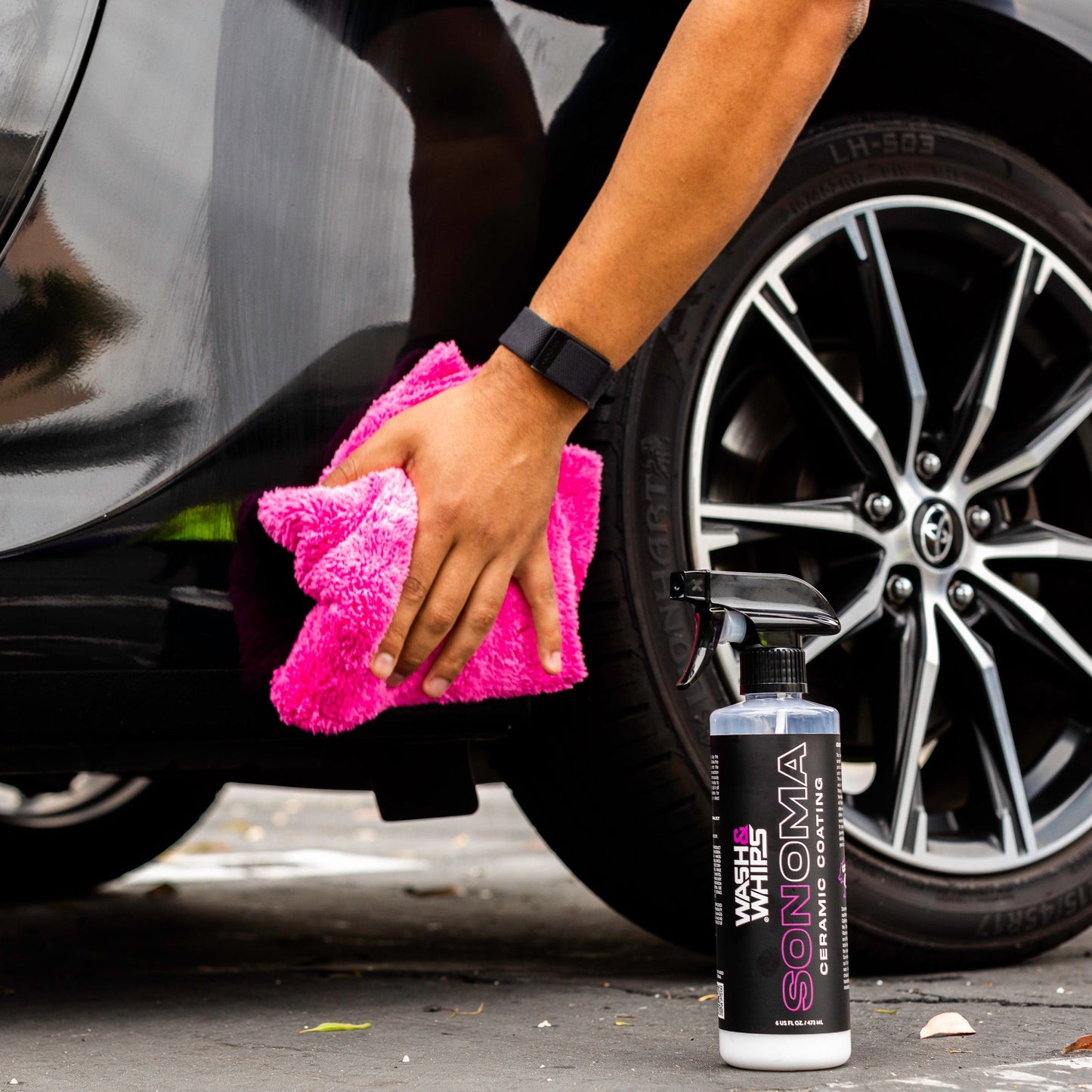 Person cleaning a car tire with a pink towel and a Sonoma car care product bottle.