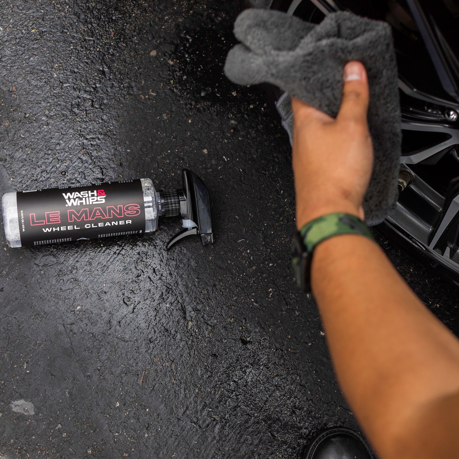 Hand holding a gray sponge next to a tube of Wheel Cleaner on a black surface