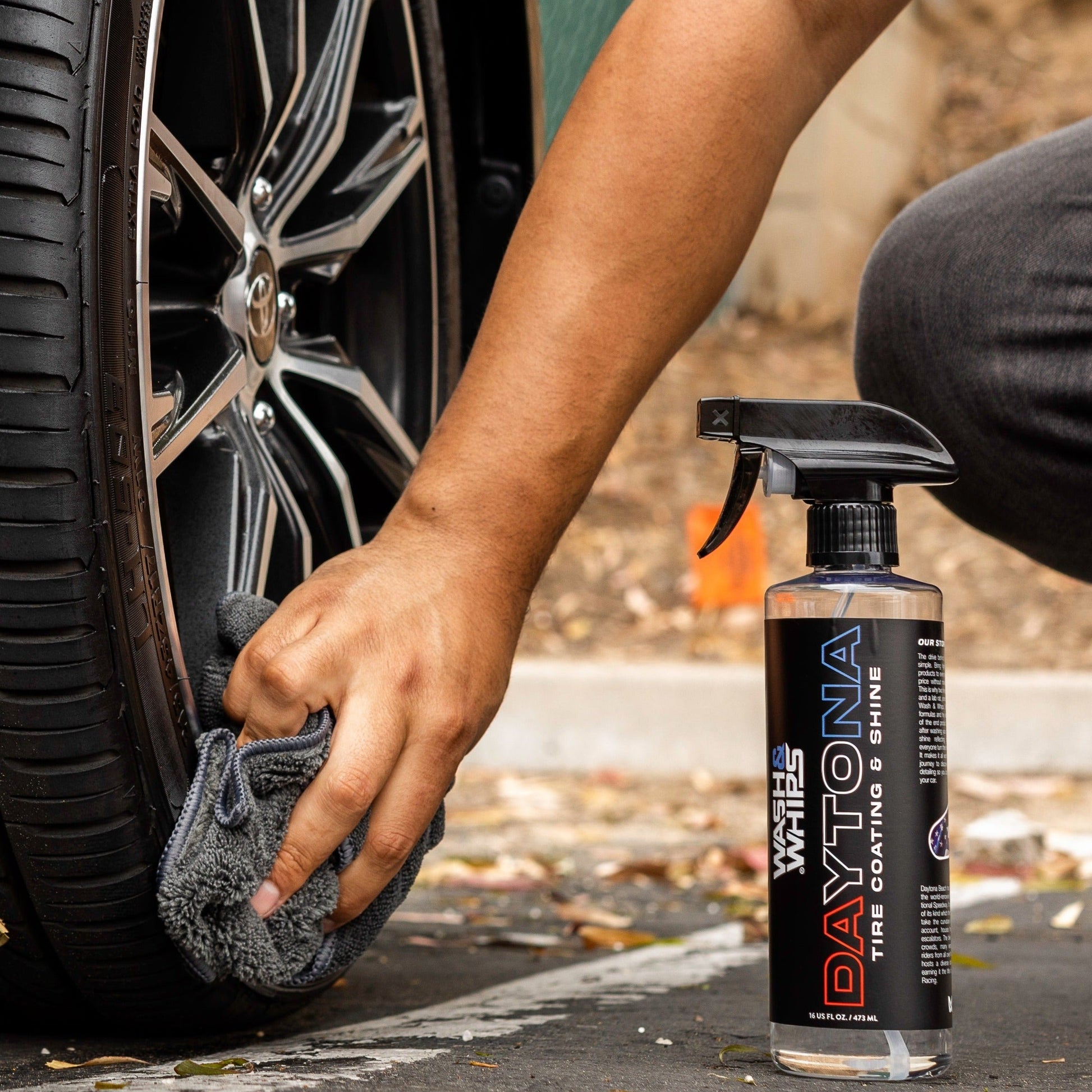 Person cleaning car wheel with a spray bottle labeled 'Daytona' and a towel.