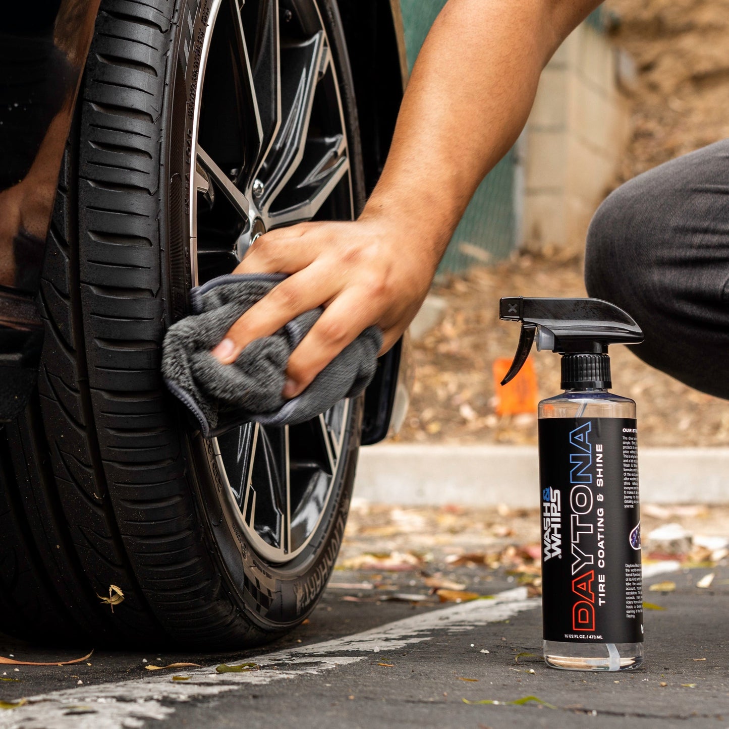 Person cleaning a car tire with a cloth, next to a bottle of Daytona Tire Dressing & Shine.