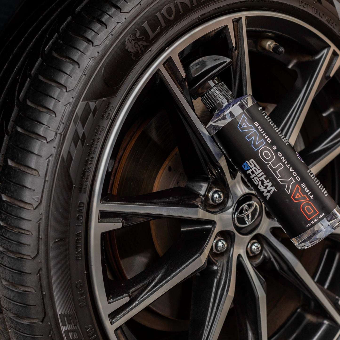 Close-up of a car wheel with a bottle of brake fluid labeled 'DAYTONA' on a black background.