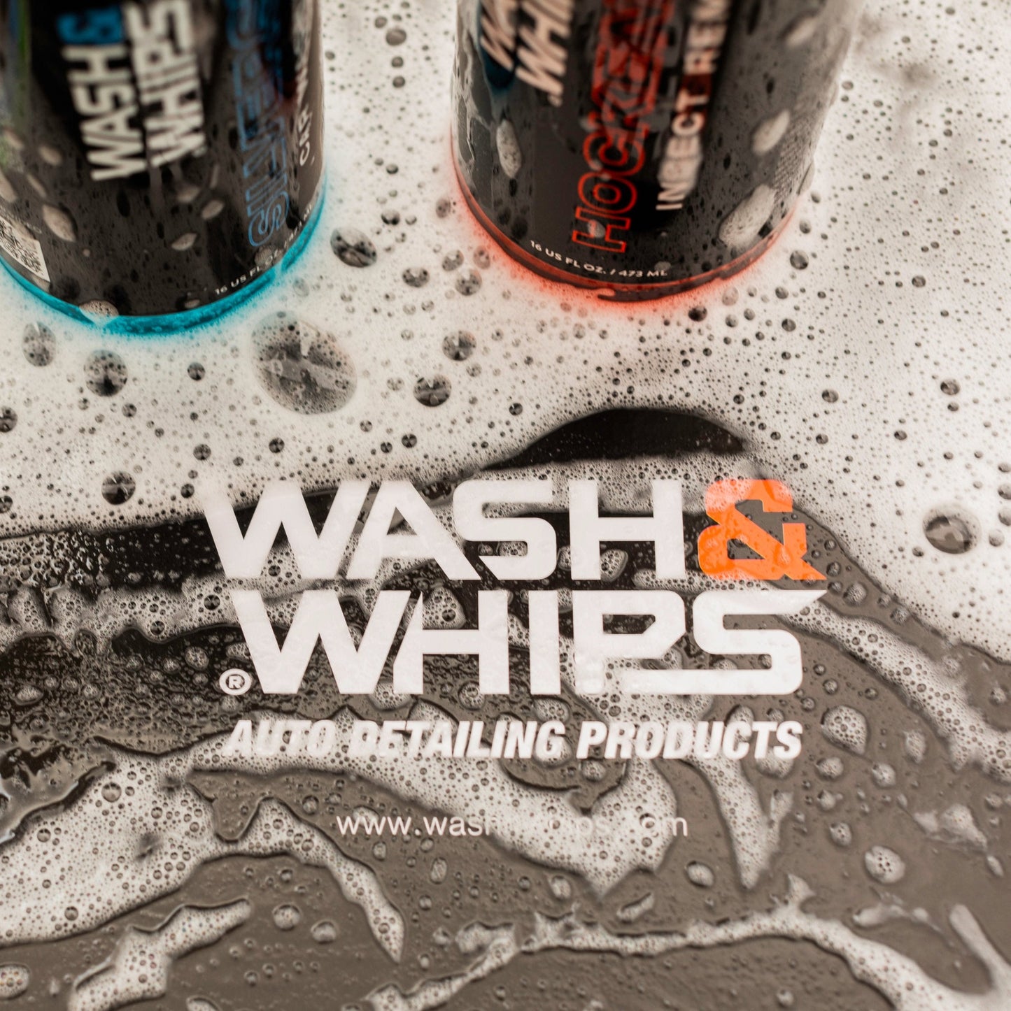 Two bottles of Wash & Whips auto detailing products on a soapy surface with the brand name displayed.