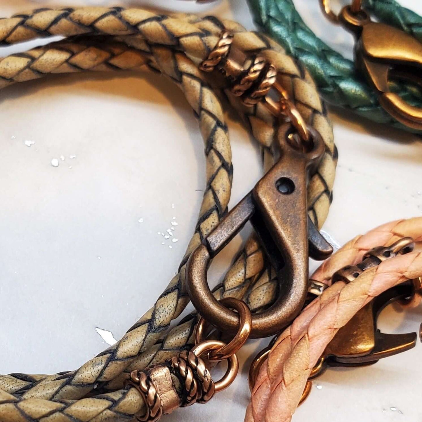 Close-up of braided leather necklaces with bronze clasps on a light background
