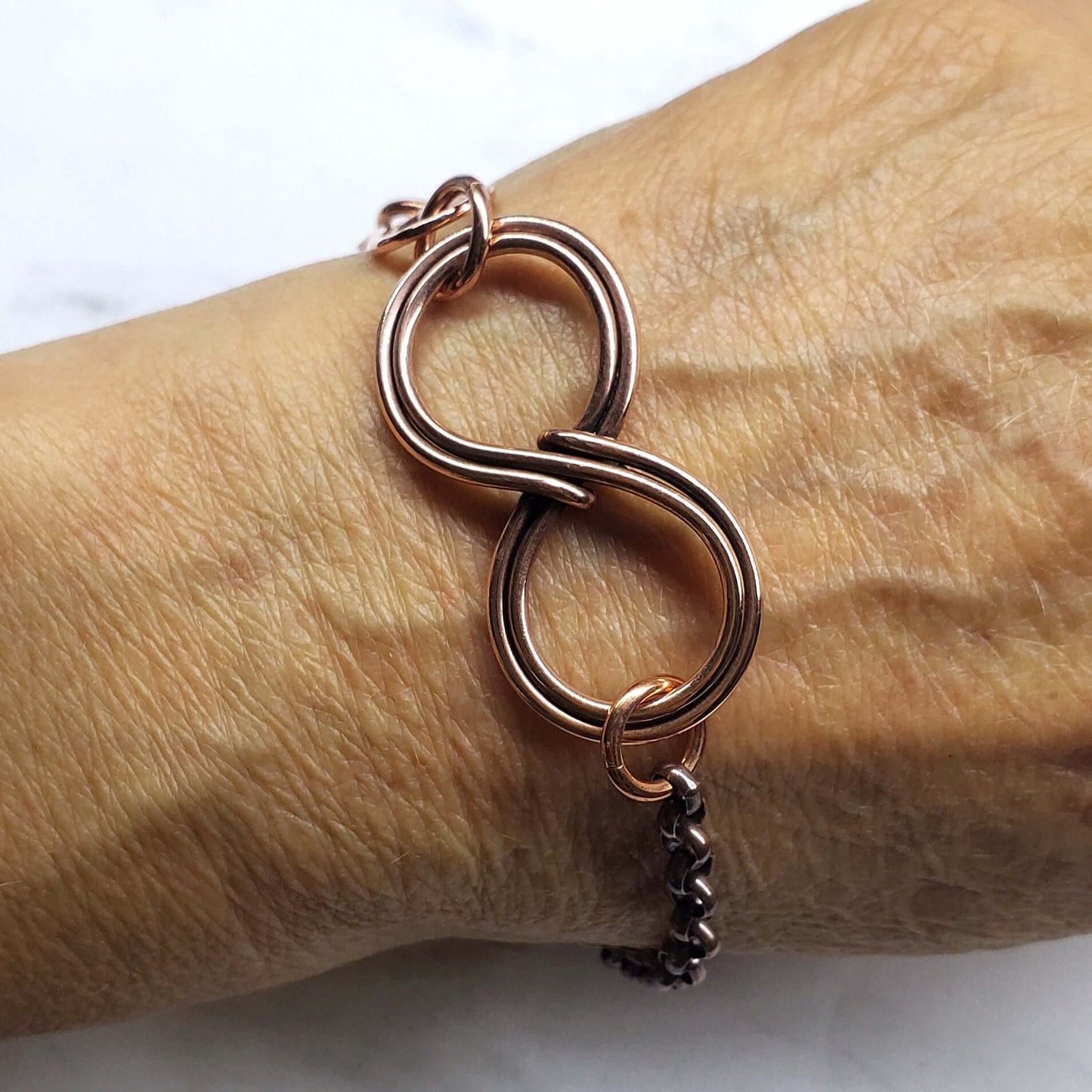 Rose gold bracelet with a chain charm on a wrist against a white background