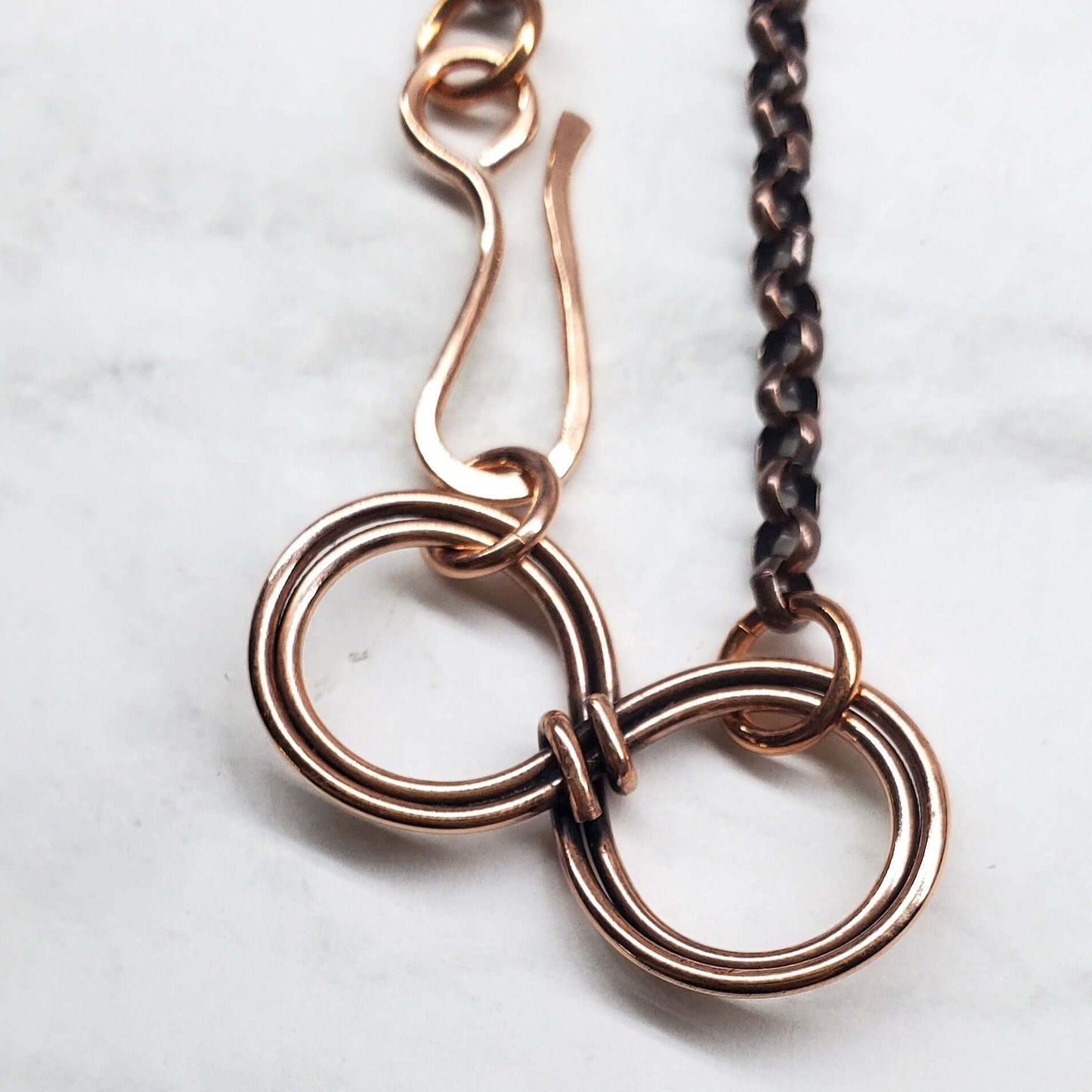 Close-up of a copper chain necklace with interlocking rings on a light background