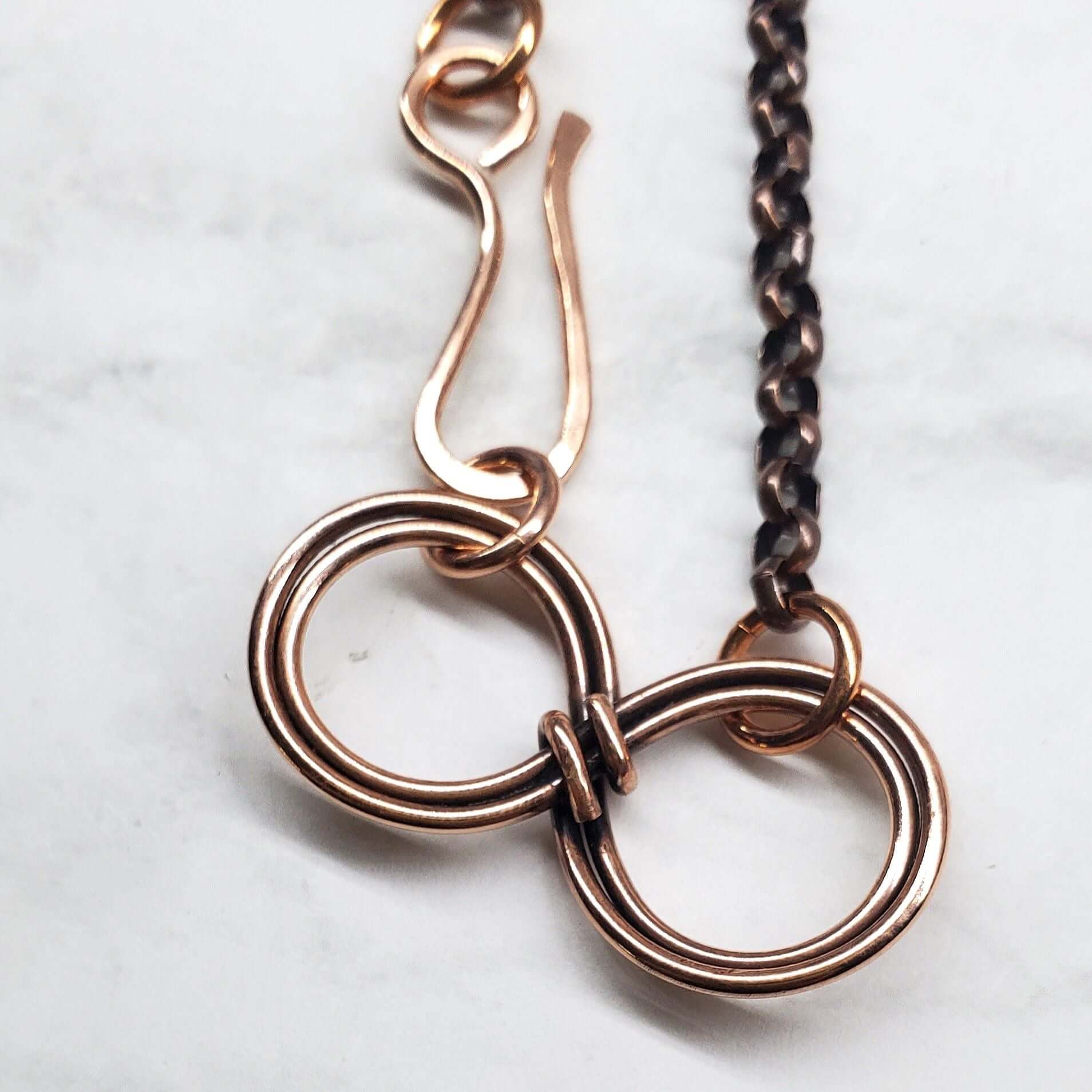 Close-up of a copper chain necklace with interlocking rings on a light background