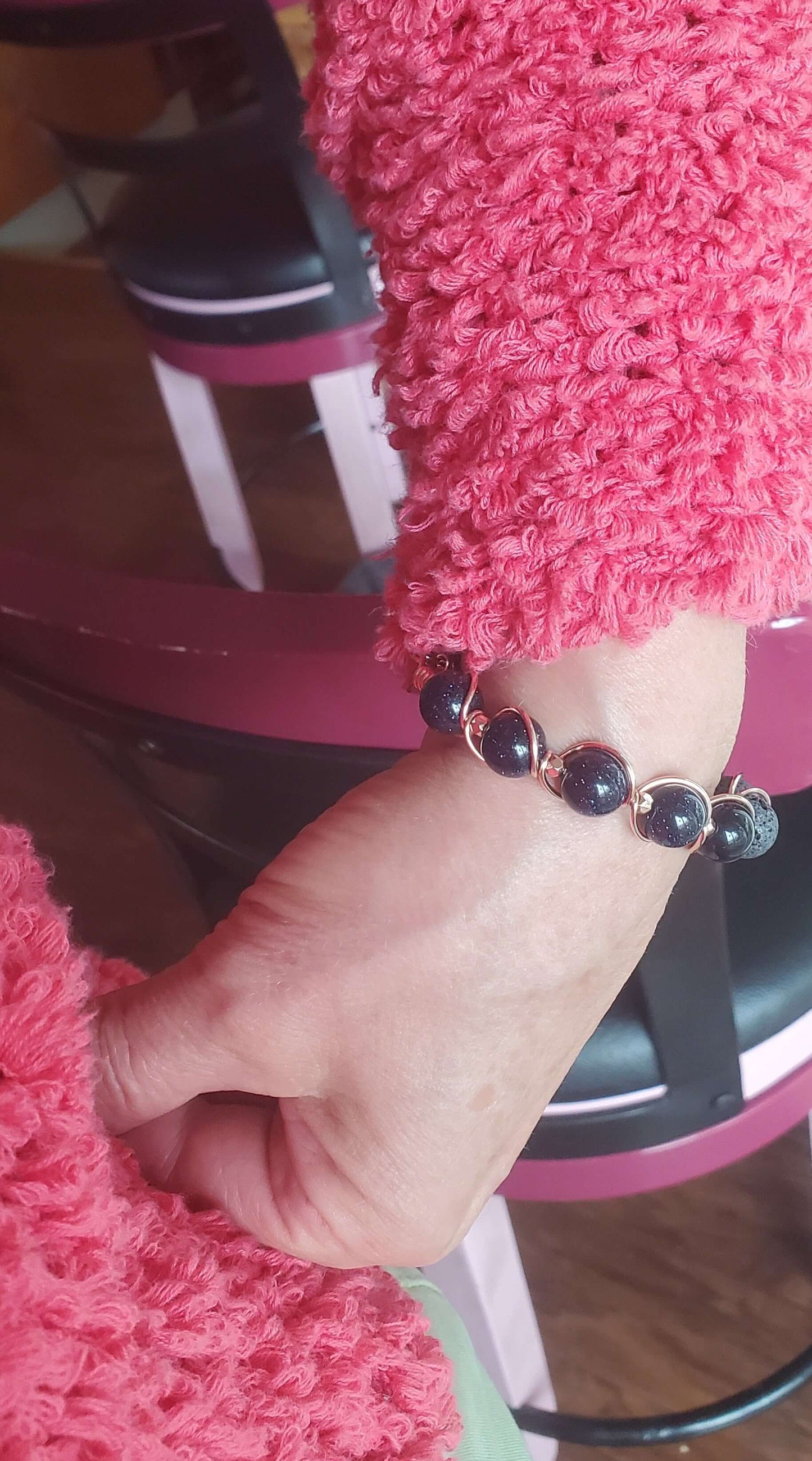 Close-up of a hand wearing a bracelet with pink fuzzy sleeves and a chair in the background.
