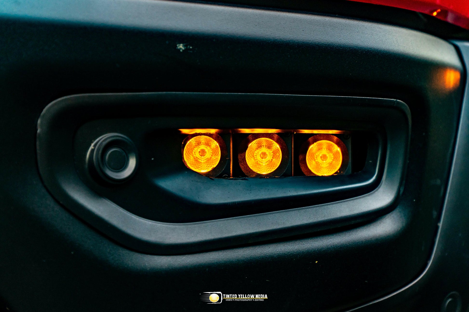 Close-up of a car's fog light with three orange lights.