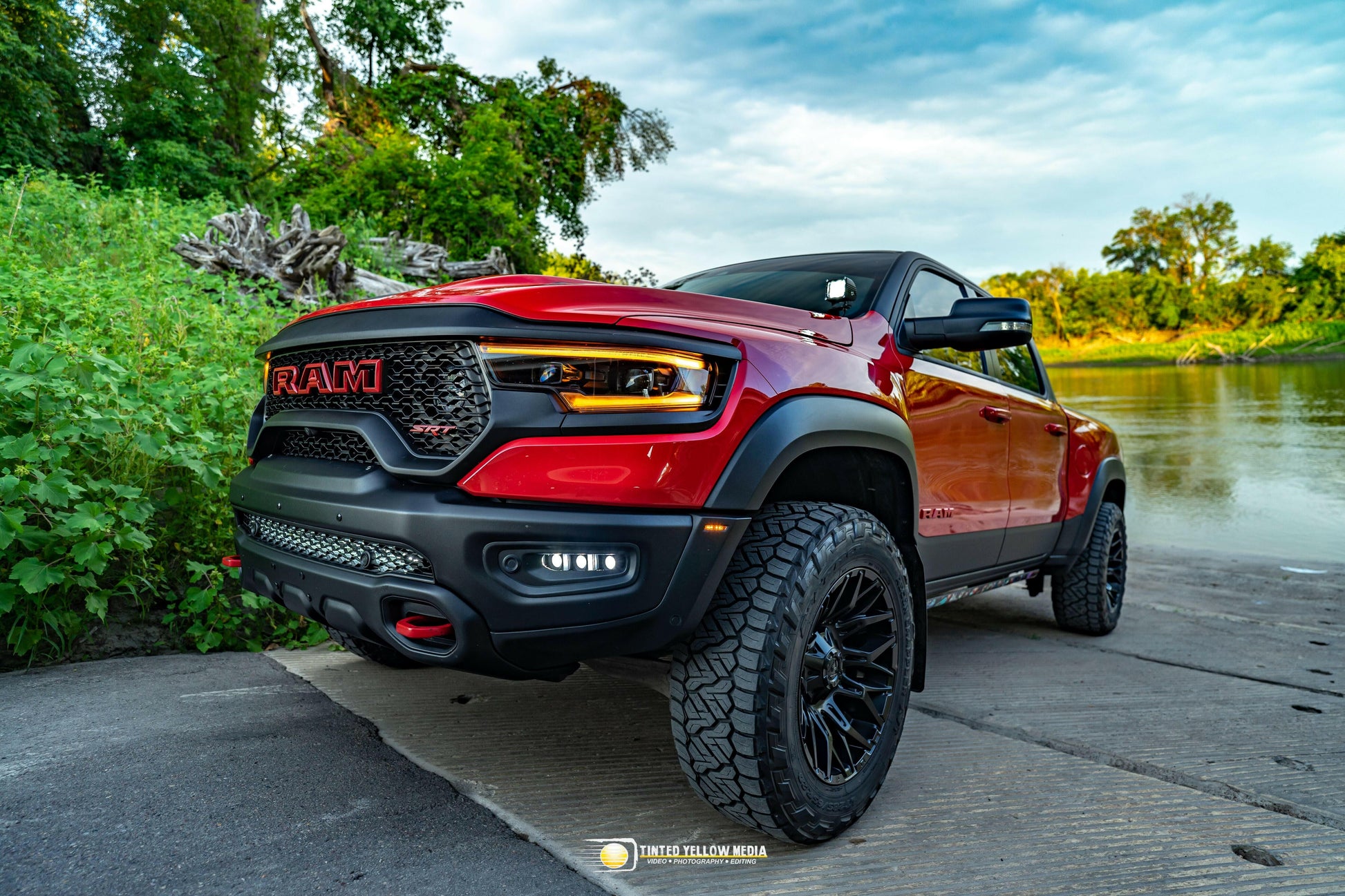 Red Ford truck parked by a body of water with greenery in the background