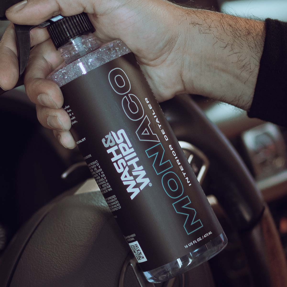 Hand holding a bottle of Monaco Interior Detailer in a car interior.