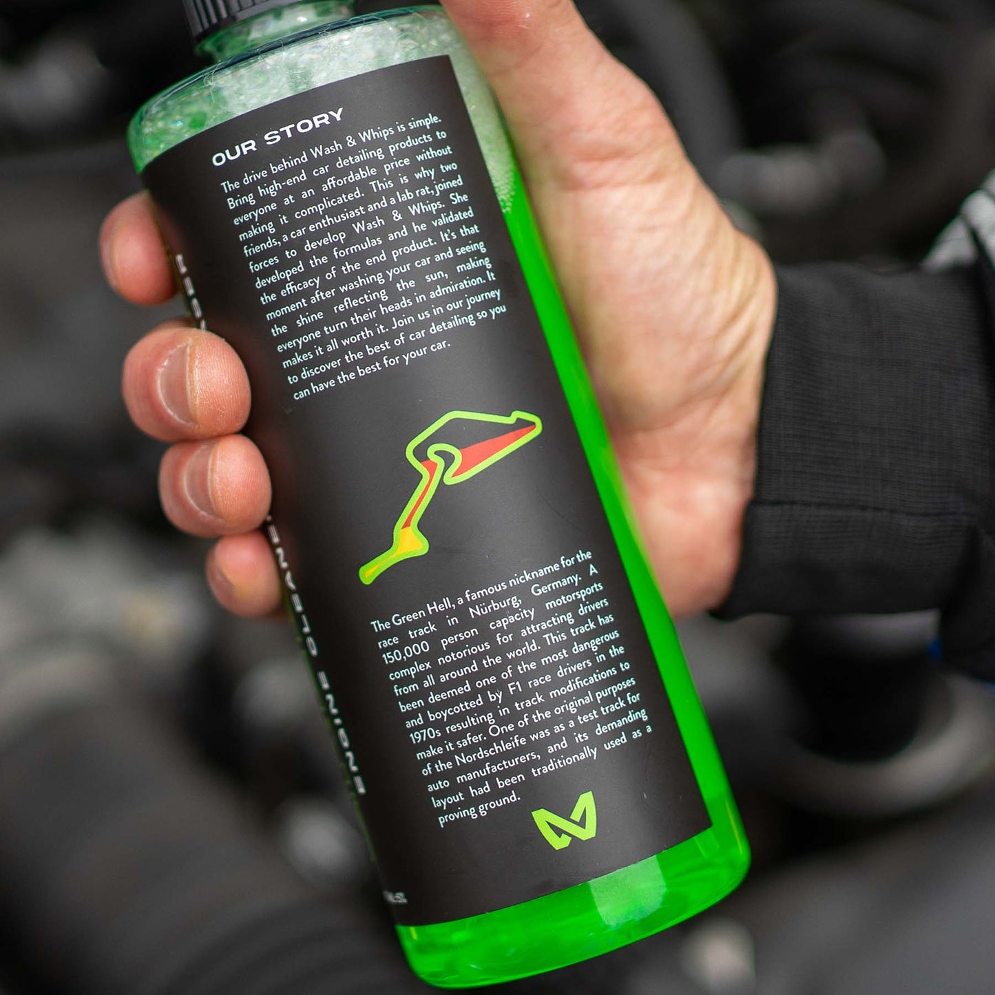 Hand holding a green bottle with text and logo, blurred background