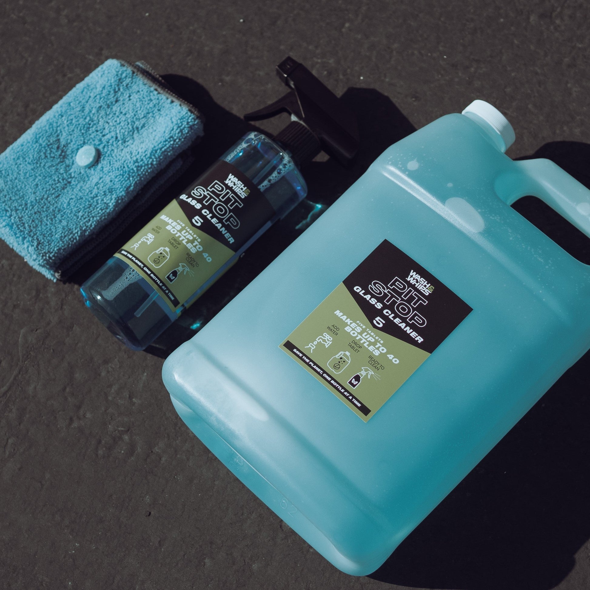 Car care products including a blue container, spray bottle, and microfiber towel on a dark surface.