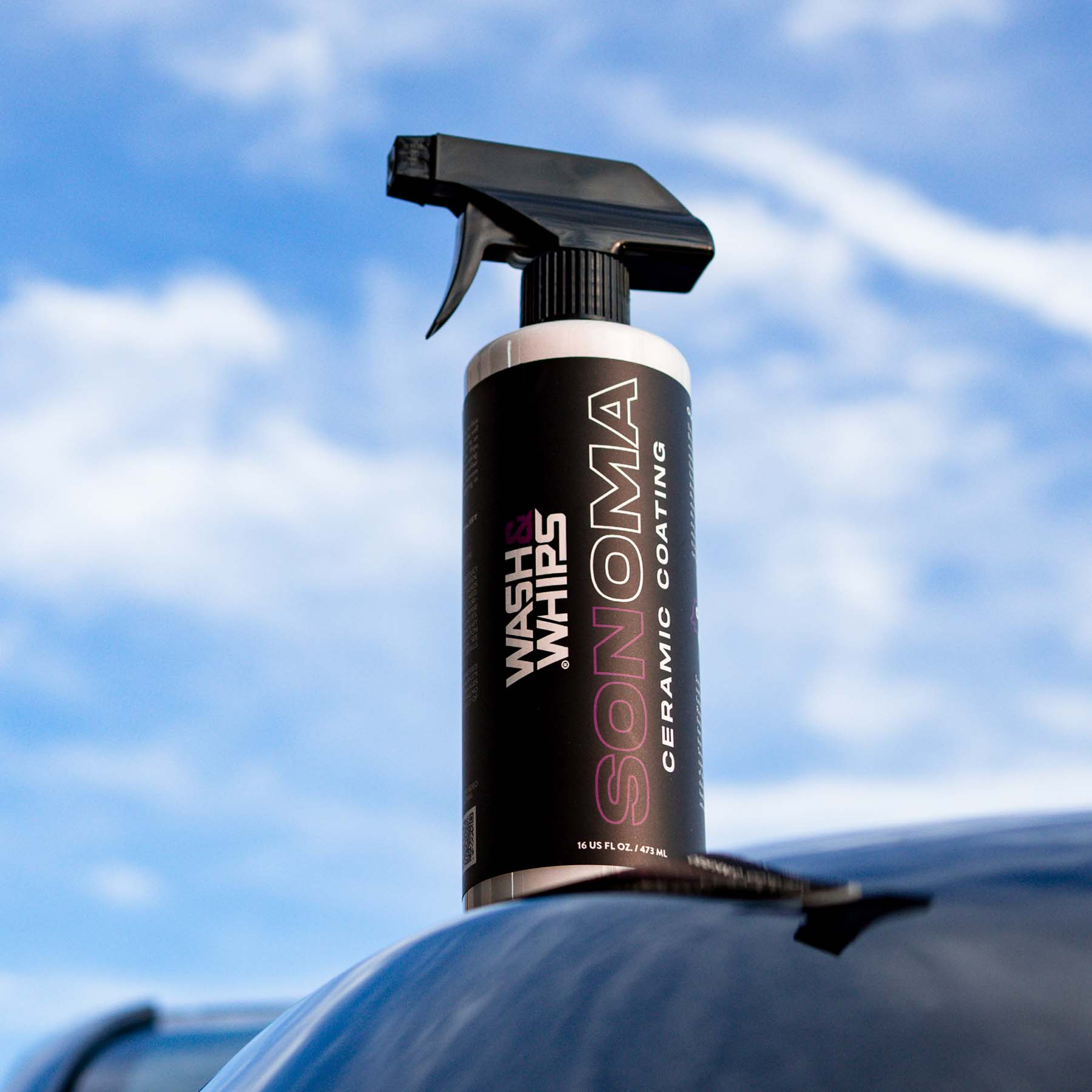 Spray bottle with 'Wash & Wax Sonoma' on a car against a blue sky.