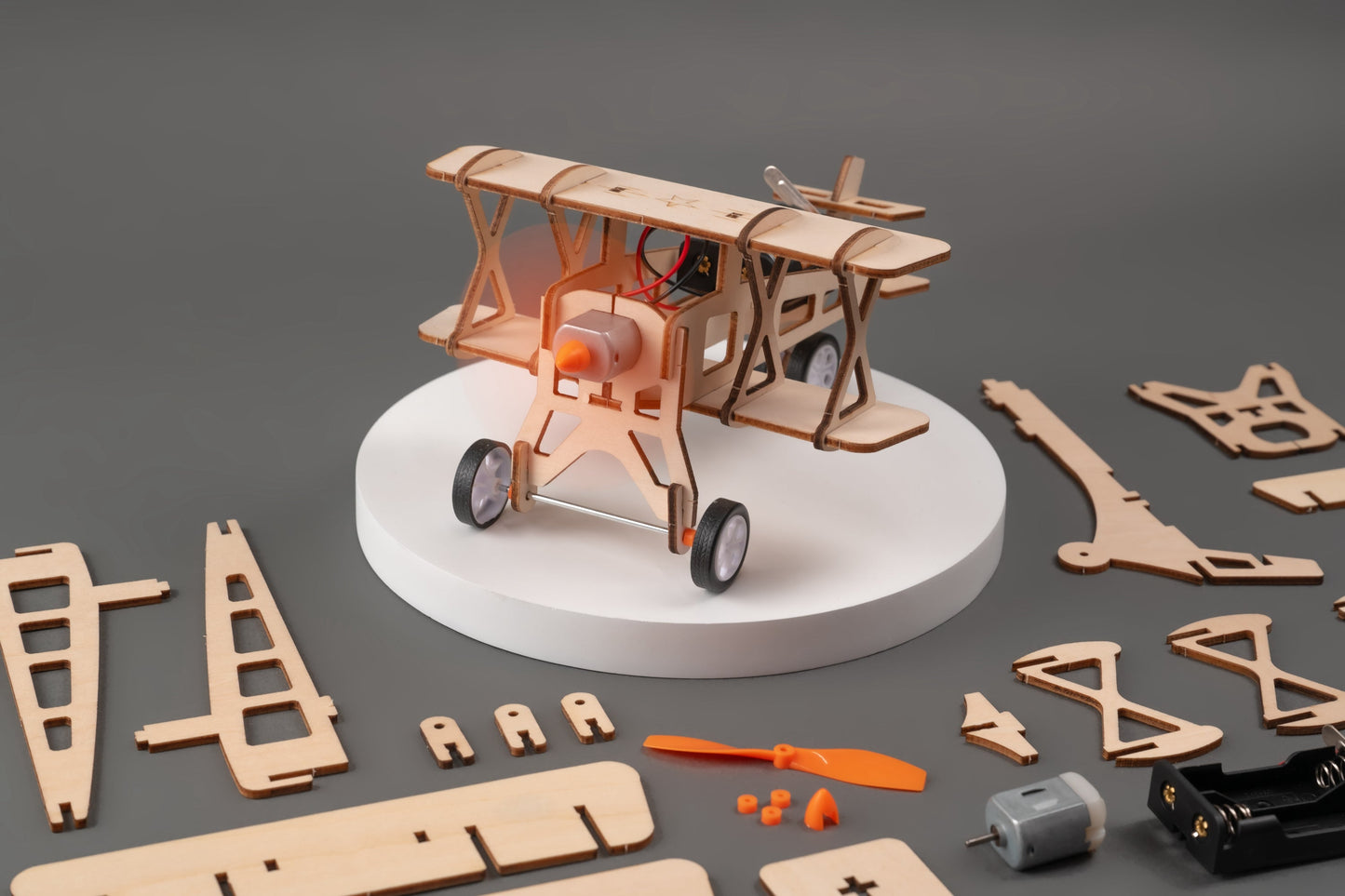 Wooden airplane model kit on a gray background with scattered parts.