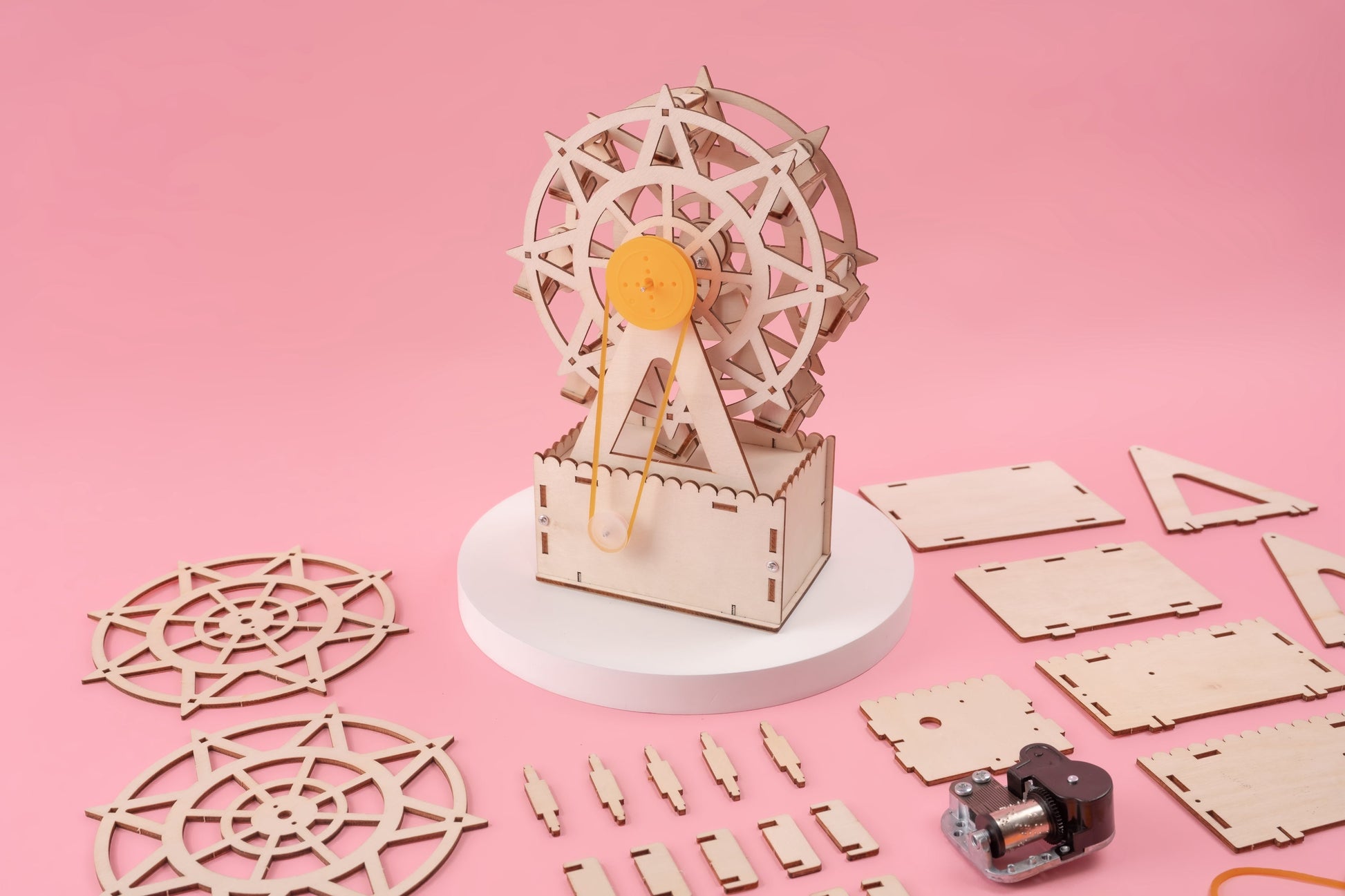 Wooden mechanical model kit with components on a pink background
